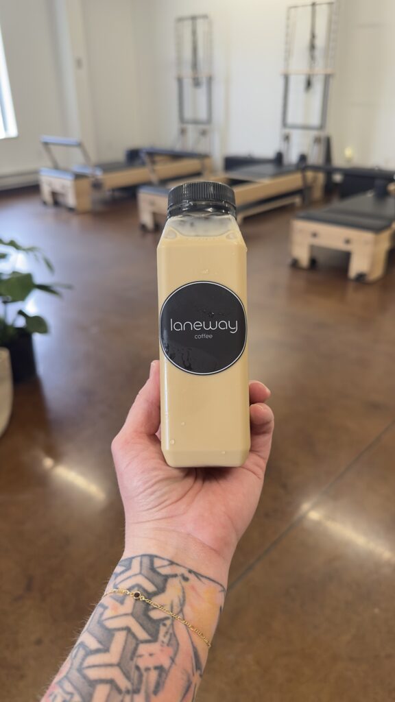 a 10oz bottle of iced vanilla coffee from Laneway Coffee Cart held in a womans hand at Powerhaus Pilates studoi